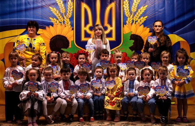Зображено дітей у вишиванках, на фоні великий прапор України з гербом України