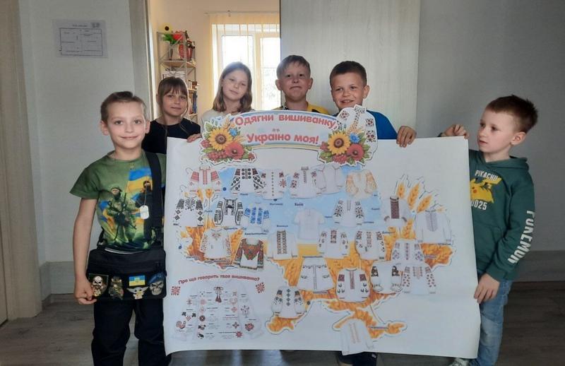 Діти тримають в руках карту України, яка складається з узорів для вишиванок з написом: "Одягни вишиванку, Україно моя!"