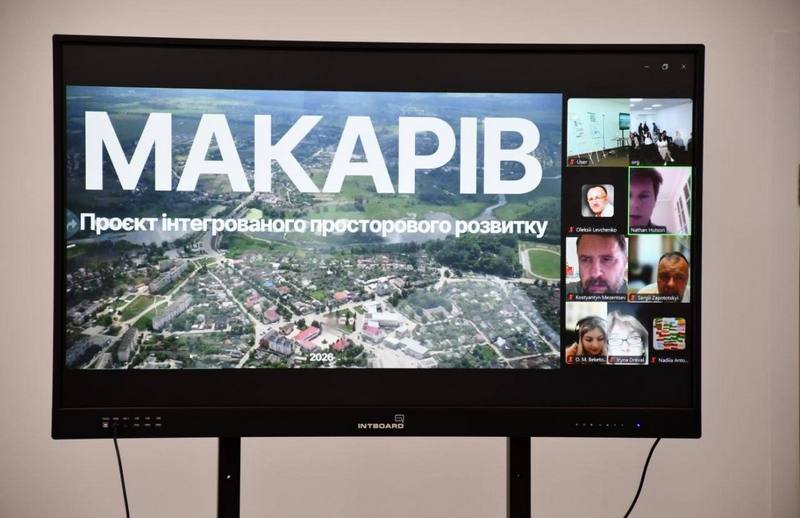 Великий інтерактивний екран у залі засідань, на якому зображено початковий слайд презентації з картою Макарова з висоти пташиного польоту та великим текстом «МАКАРІВ. Проєкт інтегрованого просторового розвитку». Справа на екрані видно вікна учасників онлайн-трансляції