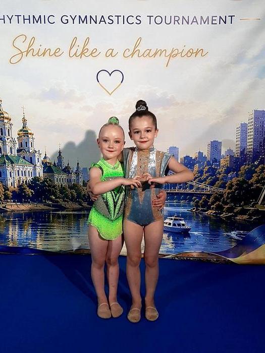 Дві юні вихованки ФСК «Макарівська громада» обіймаються та складають пальці у формі серця на тлі святкового банера