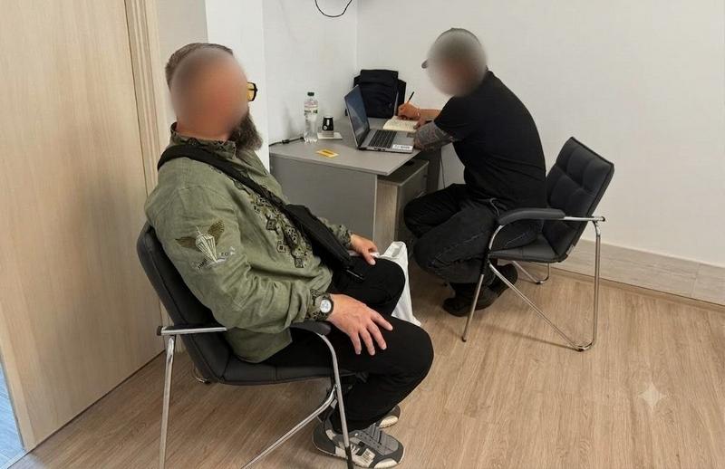 Юридична консультація ветерана. Чоловік у вишиванці хакі з військовим шевроном сидить біля робочого столу фахівця, який вносить дані в ноутбук
