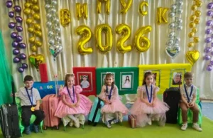 П’ятеро маленьких випускників дошкільного підрозділу Кодрянського ліцею сидять на стільчиках перед святковою фотозоною. На шиях дітей — сині стрічки з великими медалями випускників, а поруч із кожною дитиною стоїть яскрава дорожня валіза, що символізує майбутню подорож до школи. На задньому плані — золоті кульки у формі літер та цифр, які утворюють напис «ВИПУСК 2026».