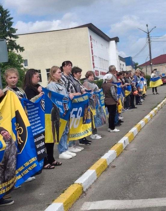 Ряди родичів і близьких полонених та безвісти зниклих військовослужбовців, які стоять уздовж вулиці під час акції підтримки, тримаючи в руках пам'ятні плакати та прапори бригад