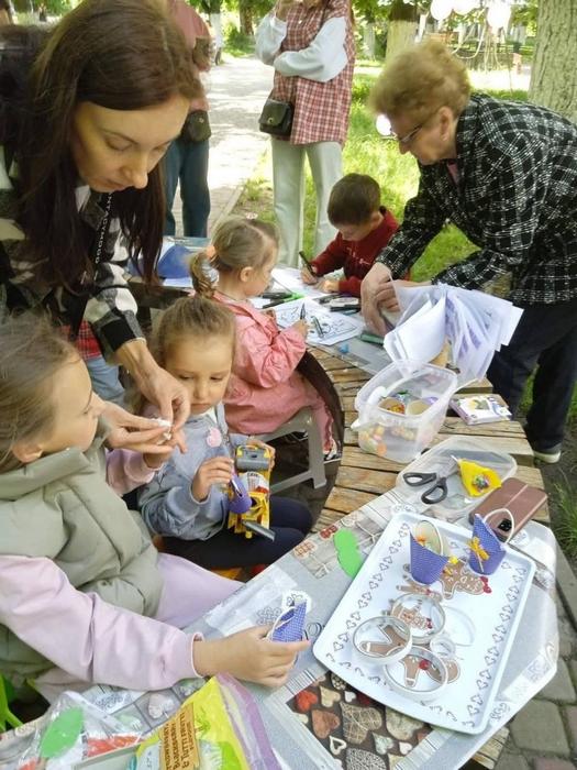 Творчий майстер-клас просто неба. Бібліотекарі допомагають дітям виготовляти паперові пороробки та малювати за столом у сквері.