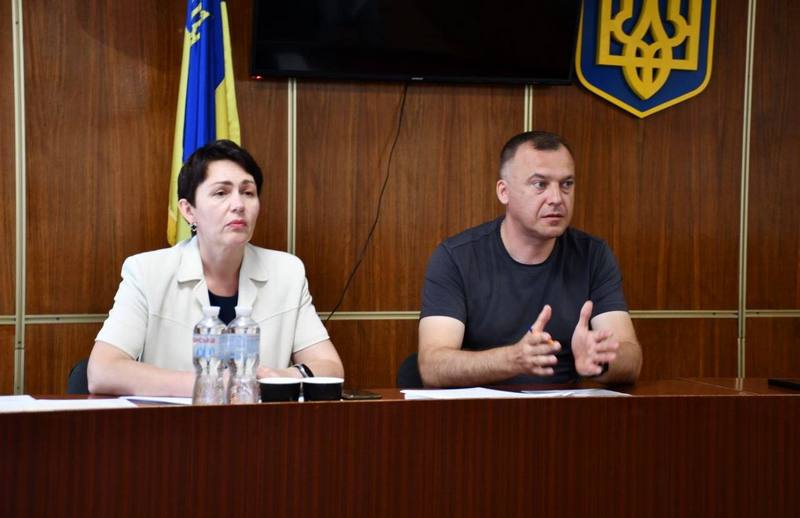 Макарівський селищний голова Вадим Токар разом із секретарем ради веде засідання сесії. Вони сидять за президією на тлі державного прапора та герба України