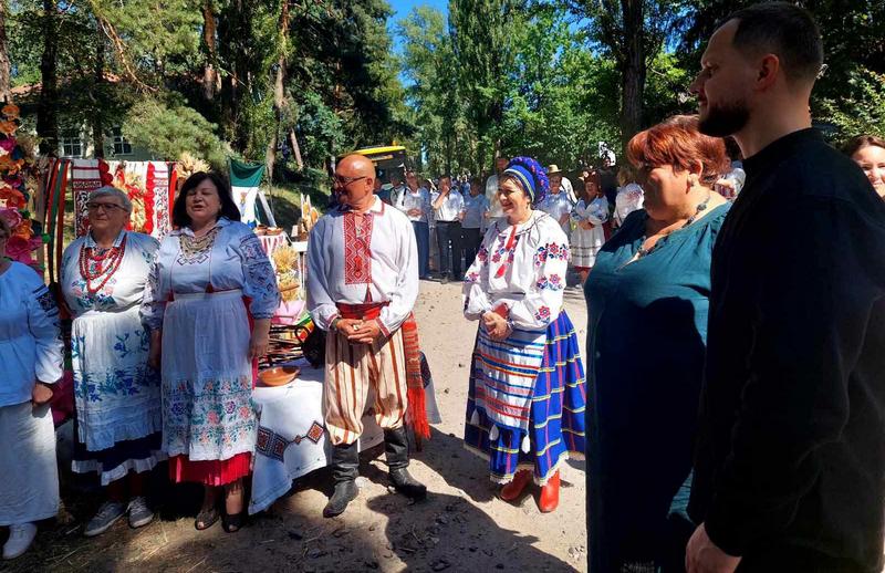 Учасники фестивалю «Київщина – земля сили» у традиційному українському вбранні на тлі виставки рушників та предметів народного побуту.
