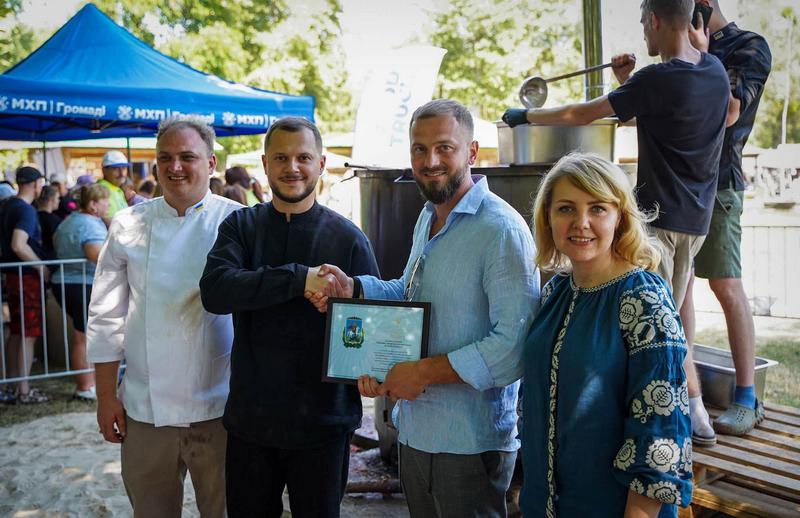 Микола Калашник, шеф-кухар Олег Бібіков та організатори заходу на тлі великого чана для приготування 1418 літрів борщу зі смаженими карасями