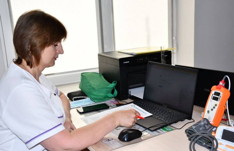Лікар в амбулаторії працює за робочим столом із ноутбуком, документами та медичним обладнанням для діагностики.