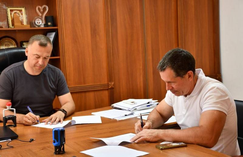 Вадим Токар та представник медичного центру сидять за столом і підписують примірники Меморандуму про співпрацю.
