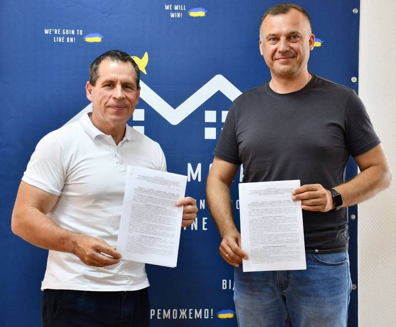 Вадим Токар та представник Національного наукового центру стоять поруч на тлі синього брендованого банера та демонструють підписані документи