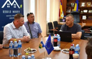 Офіційна зустріч у кабінеті: Макарівський селищний голова виступає перед польськими колегами за круглим столом із прапорами України, Польщі та ЄС. На стіні — банер благодійного фонду «Rebuild Makariv».