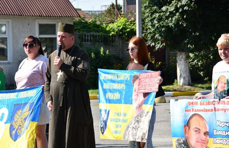 Військовий капелан виступає на акції «Їх чекають вдома», учасники тримають плакати із закликами повернути полонених бійців.