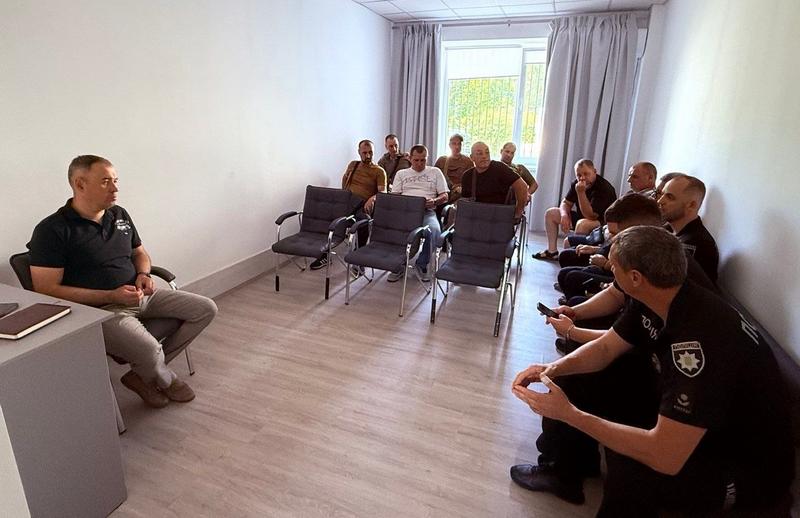 Загальний план кімнати під час зустрічі ветеранів, представників селищної ради та поліції. Учасники обговорюють питання безпеки і підтримки в Макарівській громаді.