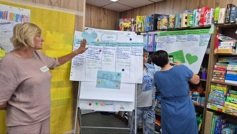 Учасниця супервізії презентує напрацювання своєї групи, вказуючи на заповнену таблицю на фліпчарті