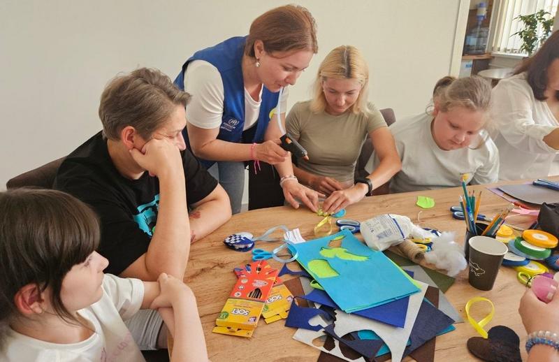 Процес створення патріотичних та символічних виробів із фетру. Фахівчиня фонду допомагає учасниці склеювати елементи за допомогою клейового пістолета.