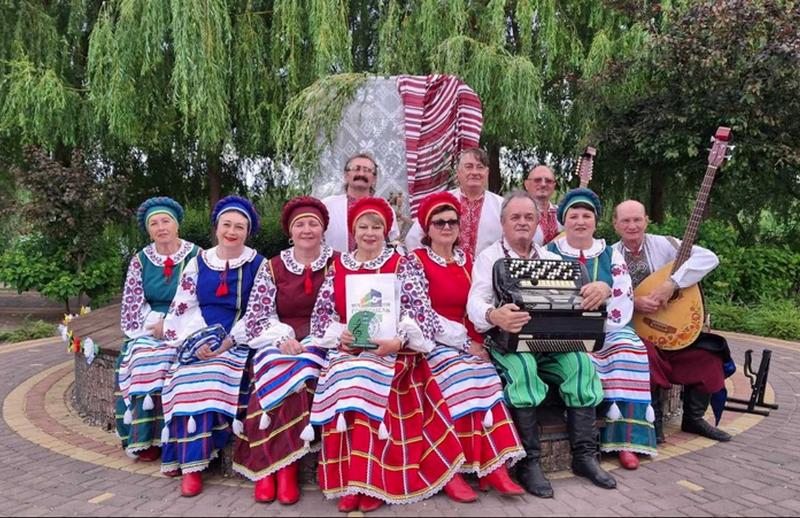 Групове фото народного аматорського ансамблю української пісні «Чебреці» у яскравих традиційних українських костюмах та з музичними інструментами на фестивалі в Гостомелі.