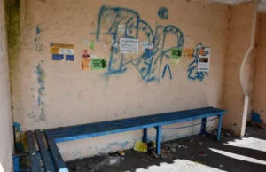 Куточок автозупинки із синьою дерев'яною лавкою, де стіни замальовані синіми графіті, а на підлозі лежать недопалки, папірці та пластикові пляшки.