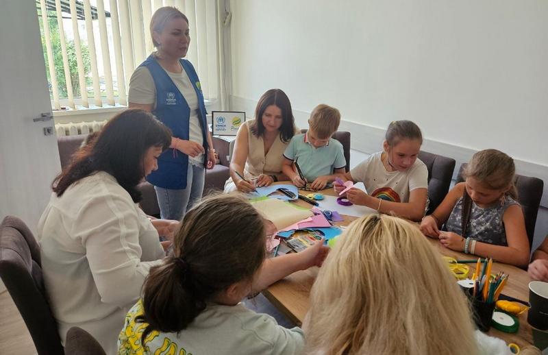 Дорослі та діти зосереджено працюють за столом із фетром, стрічками та олівцями під час майстер-класу «У візерунках родинного тепла».