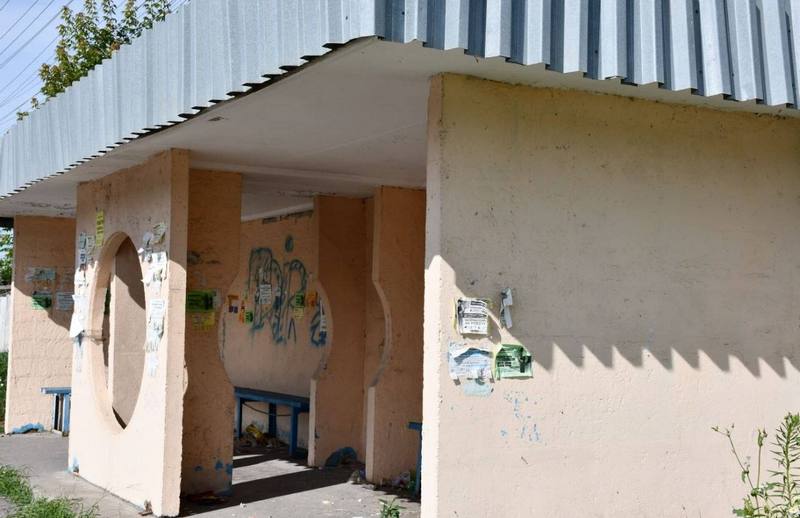 Загальний вигляд понівеченої громадської зупинки транспорту в громаді. Стіни розмальовані графіті, наклеєні хаотичні оголошення.