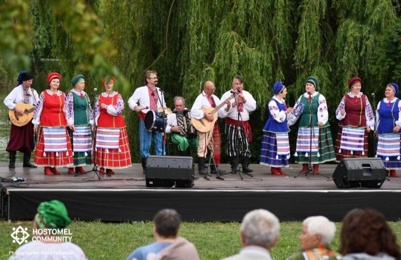 Виступ ансамблю «Чебреці» на літній сцені фестивалю «Відомі пісні мого краю» в Гостомелі перед глядачами. Учасники співають та грають на народних інструментах.