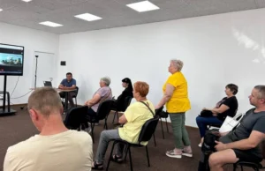 Учасники обговорення різного віку сидять у кабінеті зі світлими стінами та уважно слухають представників селищної ради та консультантів проєкту HOPE.