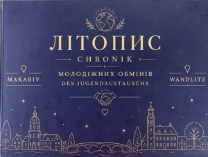 Темно-синя обкладинка книги з золотим написом «Літопис молодіжних обмінів Макарів — Вандліц» двома мовами (українською та німецькою), прикрашена ілюстраціями рукостискання, земної кулі та силуетами архітектури обох міст.