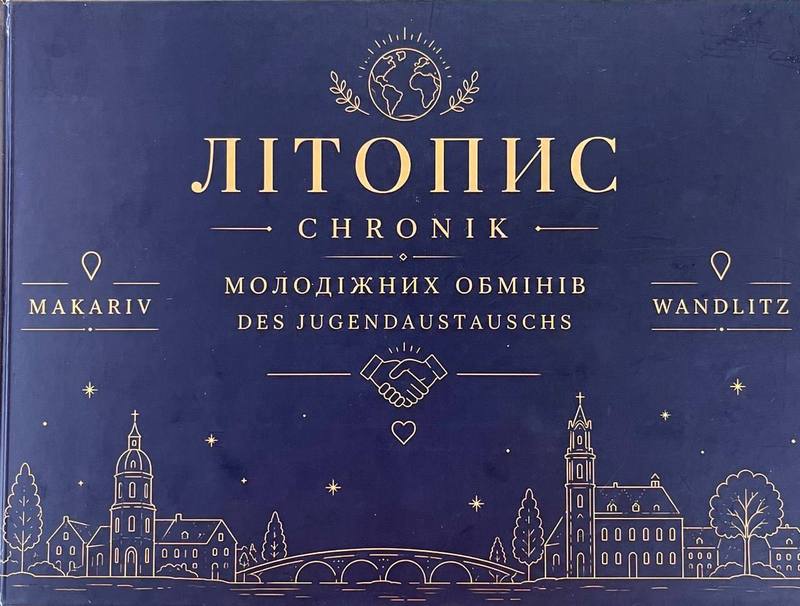 Темно-синя обкладинка книги з золотим написом «Літопис молодіжних обмінів Макарів — Вандліц» двома мовами (українською та німецькою), прикрашена ілюстраціями рукостискання, земної кулі та силуетами архітектури обох міст.
