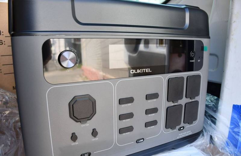 Крупний план портативної зарядної станції сірого кольору бренду 'OUKITEL'. Видно дисплей, ручку регулювання та численні порти (USB, AC, DC) для підключення пристроїв.