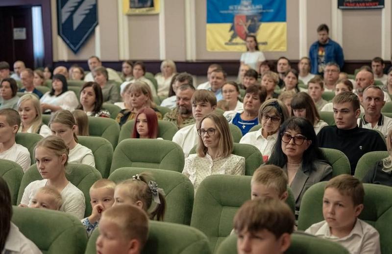 Глядацька зала обласної конференції «Жінки, мир, безпека», заповнена людьми різного віку. На задньому плані видно Державний Прапор України та прапор Київської області.
