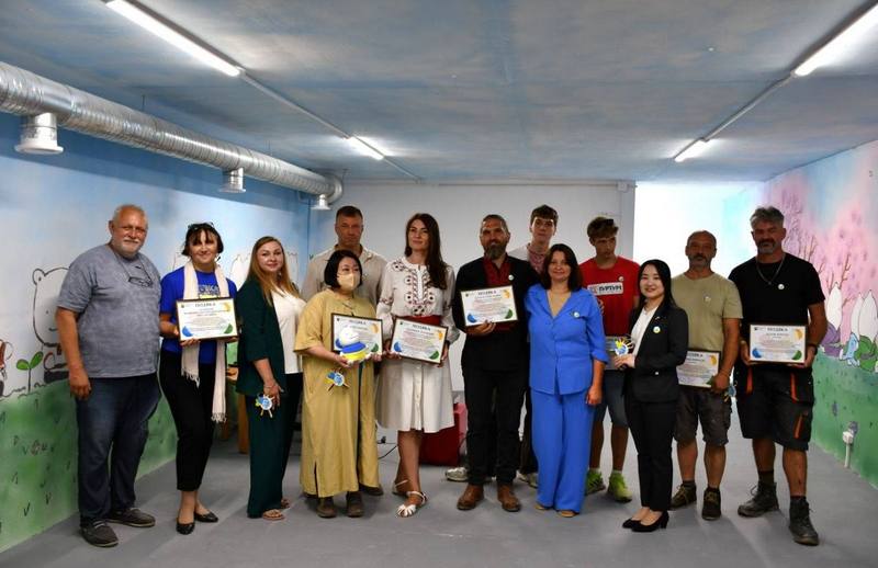 Офіційні гості, представники Посольства Японії, БФ «ГУРТУМ», місцевої влади та волонтери тримають у руках подяки та грамоти під час урочистого відкриття укриття дитячого садка в Колонщині.