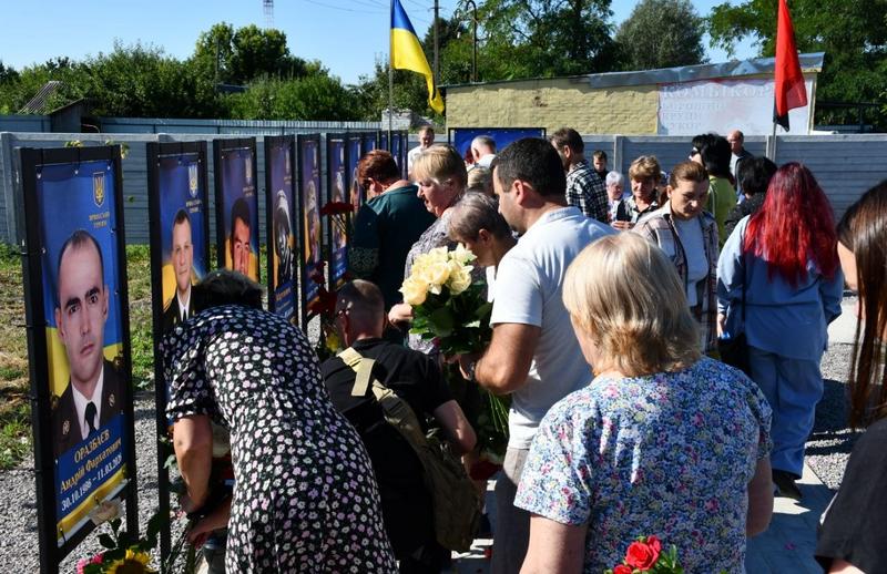 Мешканці громади покладають квіти до освячених портретів загиблих воїнів на Алеї пам'яті у Фасівочці. Крупним планом видно стенд із фотографією Андрія Оразбаєва, до якого прийшли вшанувати пам'ять.