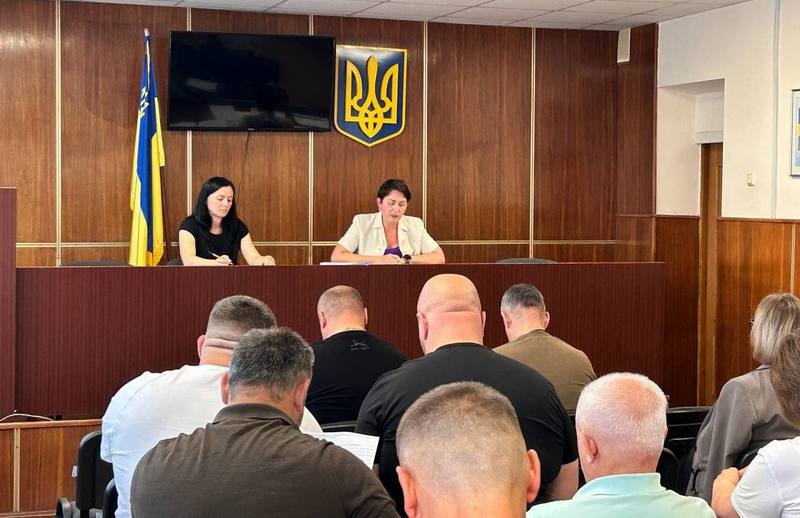 Засідання президії Макарівської селищної ради. У центрі за столом — головуюча на засіданні, поруч — секретар. Позаду них на стіні — Державний Герб України та прапор України. Спереду — депутати, які слухають виступ.
