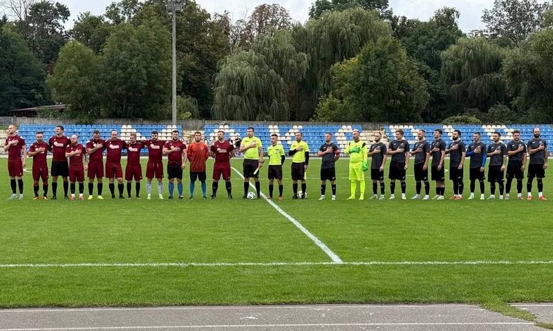 Футболісти ФСК «Макарів», СК «Юрівка» та арбітри шеренгою стоять на полі стадіону під час виконання Гімну України перед початком матчу.