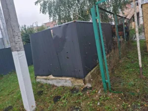 Темно-сіра металева споруда з чисельними отворами від уламків та пробитою стінкою за сітчастою огорожею на території закладу.
