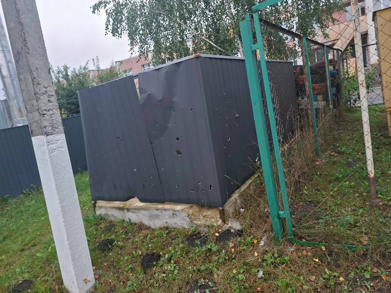 Темно-сіра металева споруда з чисельними отворами від уламків та пробитою стінкою за сітчастою огорожею на території закладу.