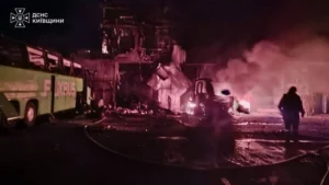 Ліквідація пожежі підрозділами ДСНС після влучання БПЛА в селі Копилів: палаюча будівля СТО, пошкоджені автобус FlixBus і вантажівка, силает рятувальника на тлі диму.