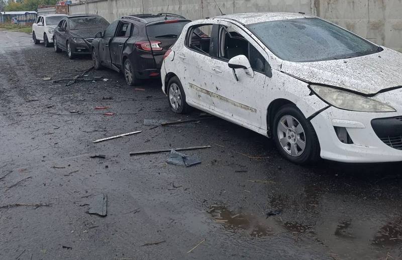 Чотири пошкоджені автомобілі стоять у ряд на дорозі. Кузов білої машини на передньому плані вкритий осколковими пошкодженнями та пилом, а на асфальті навколо розкидані дрібні уламки.