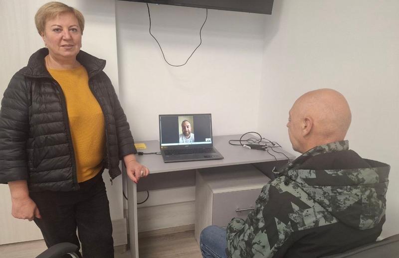 Ветеран сидить перед ноутбуком під час онлайн-консультації з юристом, поруч із ним у кабінеті ветеранського простору «Серед Своїх» стоїть адміністратор простору.