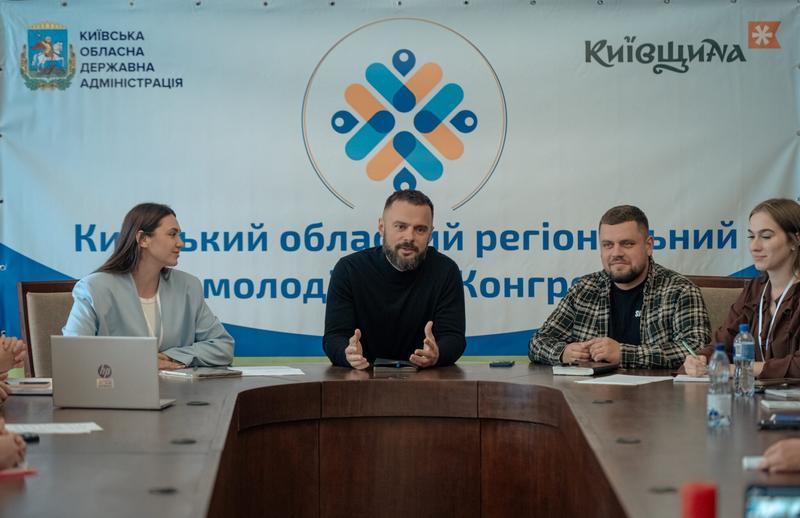Заступник голови Київської ОДА Іван Добровольський виступає перед учасниками засідання Регіонального молодіжного конгресу Київщини. Поруч за столом — учасники президії на тлі баннера заходу.