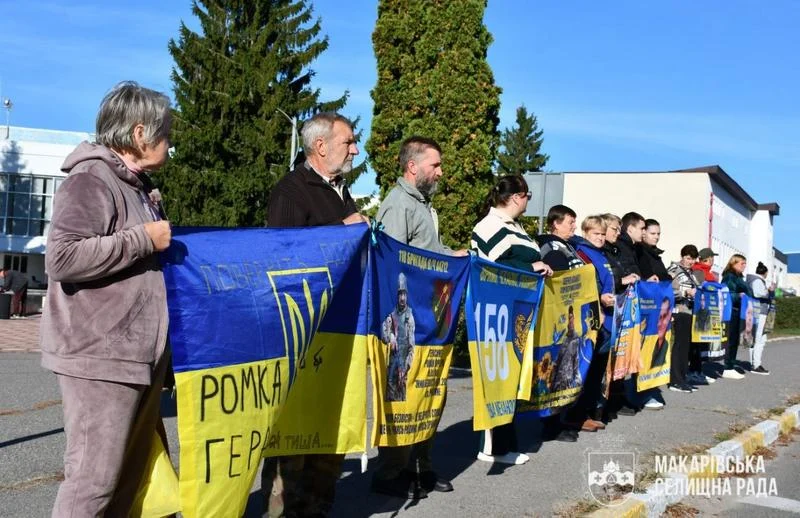 Учасники мирної акції стоять уздовж дороги з синьо-жовтими плакатами та прапорами на підтримку зниклих безвісти й полонених українських військових.
