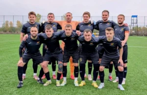Гравці футбольної команди ФСК «Макарів» у темній формі позирують для командного фото на футбольному полі перед початком гри.