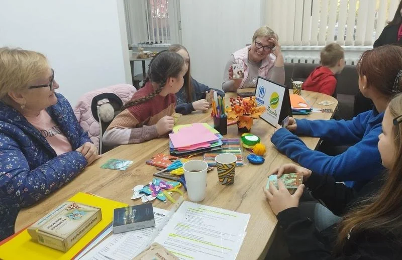 Учасники зустрічі сидять за столом у затишній атмосфері ветеранського простору «Серед Своїх», спілкуються та розглядають картки під час розвивального заняття.